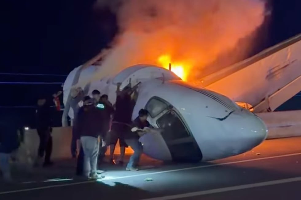 Varias personas intentan sacar a los pasajeros de un avión tras estrellarse este en una...